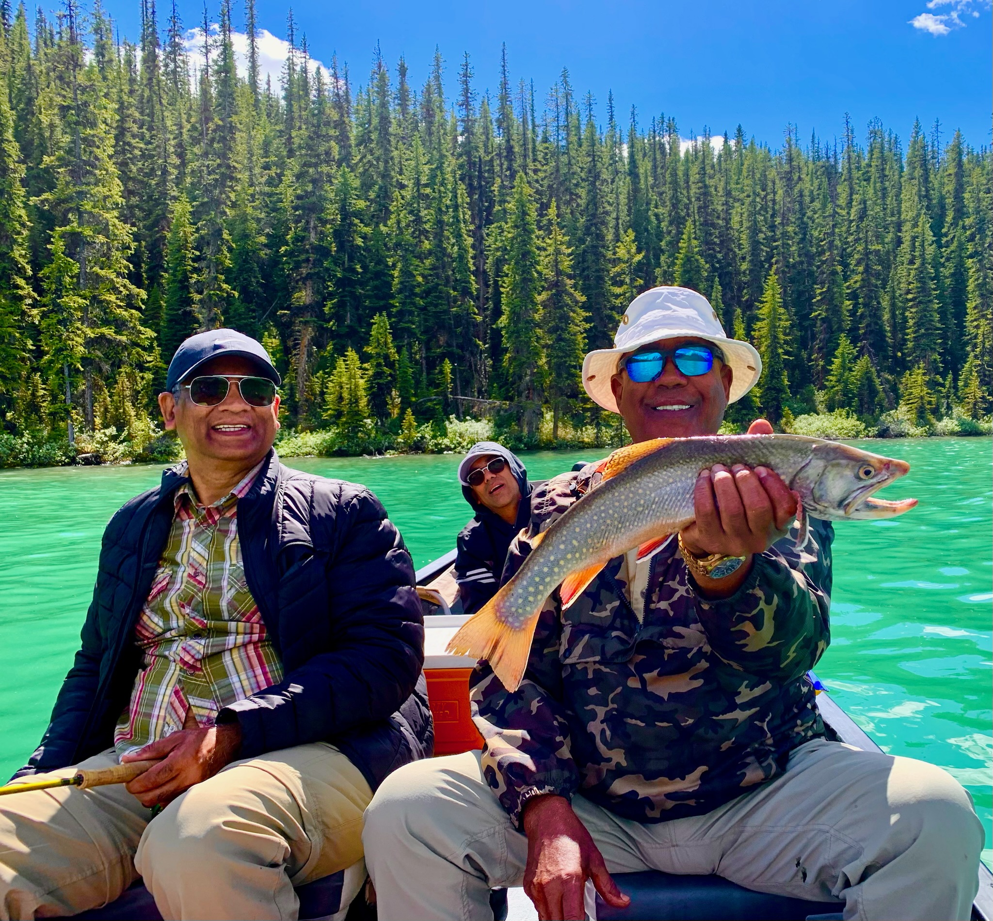 Three anglers on boat holding lake trout on emerald Maligne Lake, guided fishing Jasper National Park