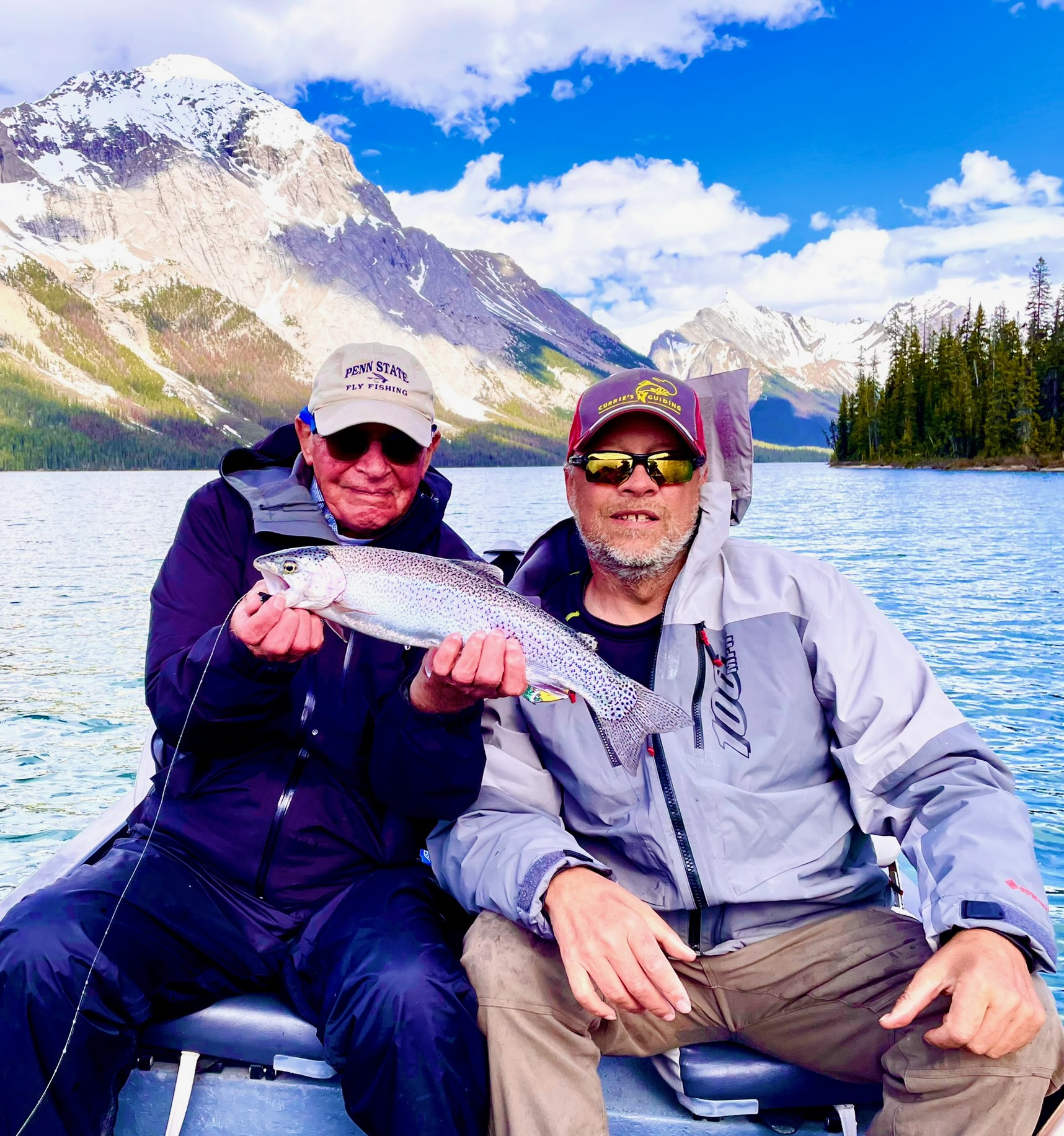 Guide and guest holding rainbow trout with dramatic snowy Maligne Lake mountains