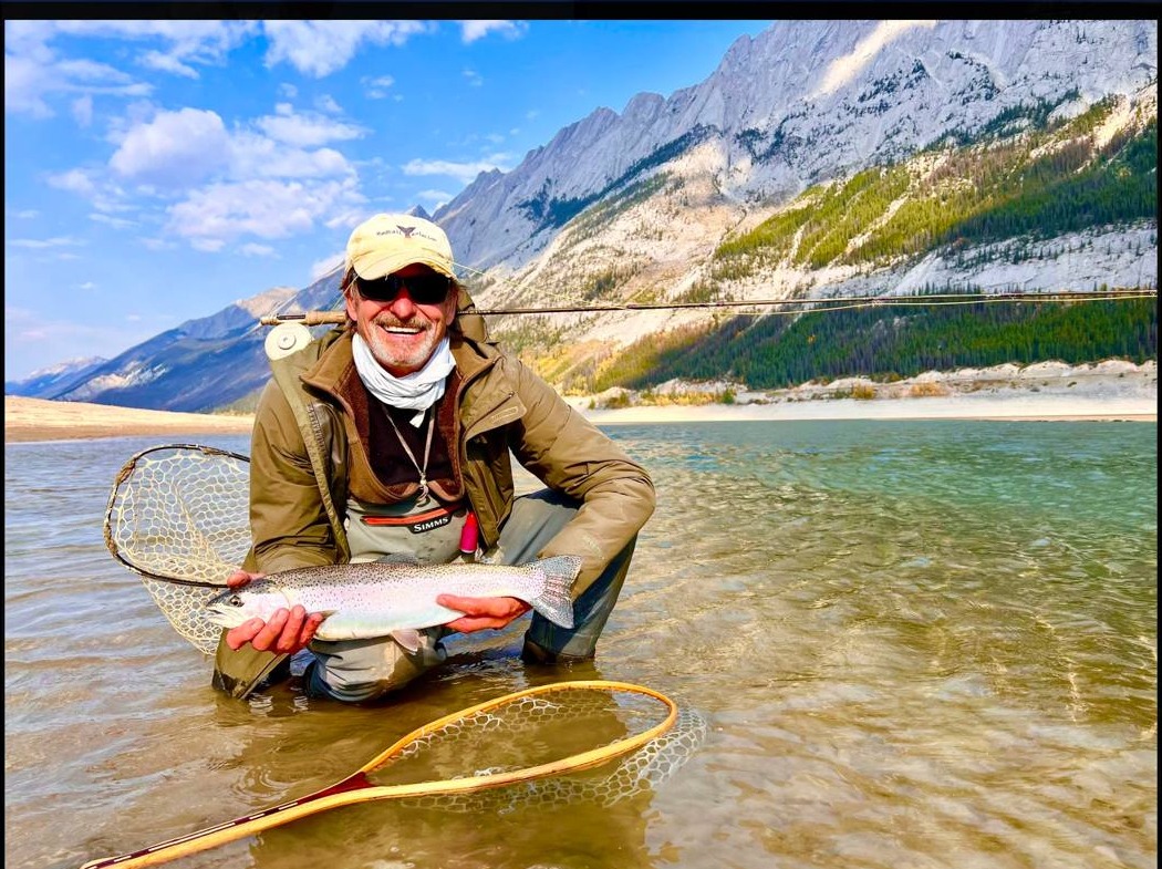 Angler wade fishing Medicine Lake with dramatic limestone peaks, Jasper National Park