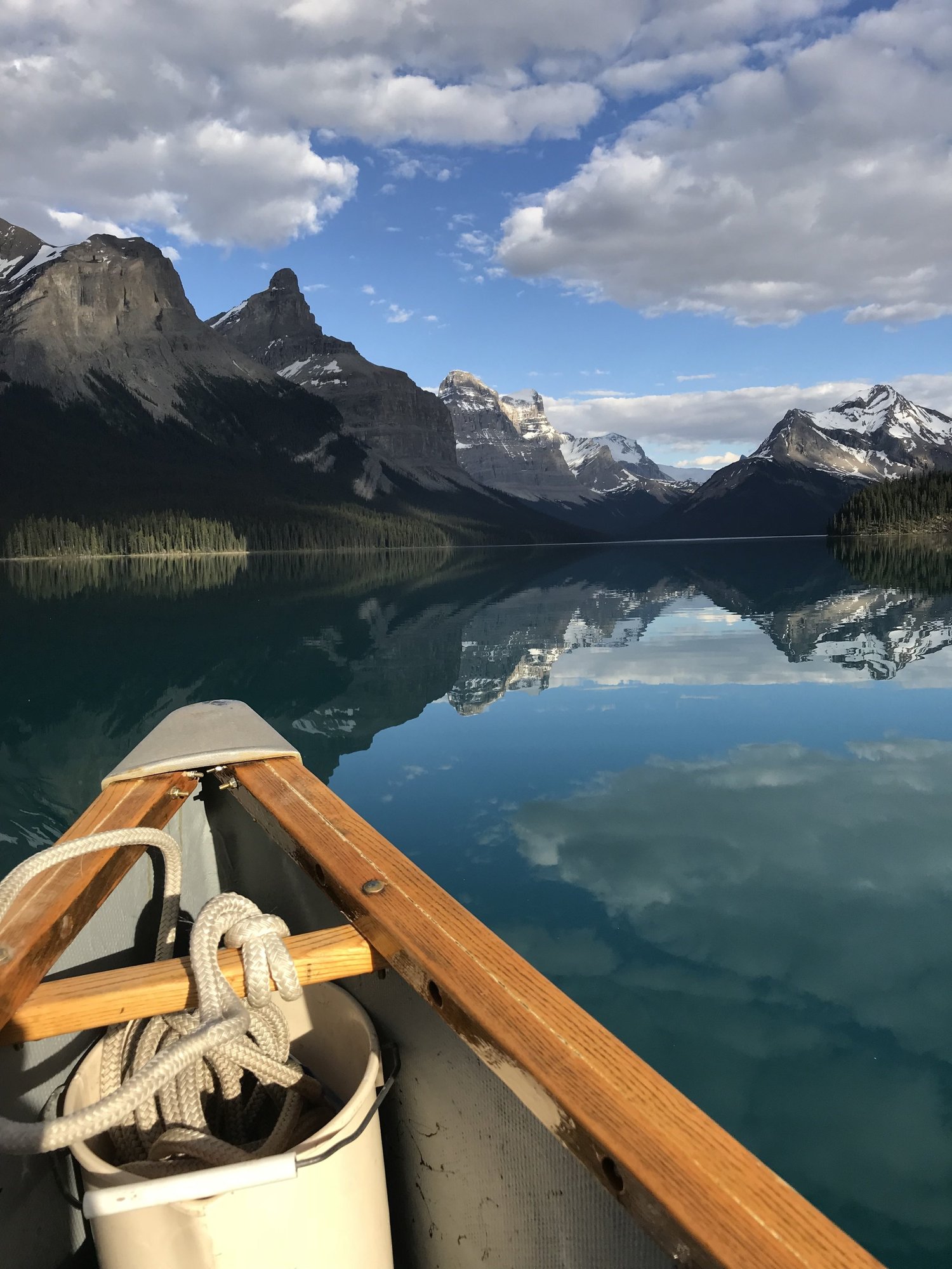 View from canoe bow on mirror-calm Maligne Lake with Rocky Mountain peaks reflected in the water, Jasper National Park